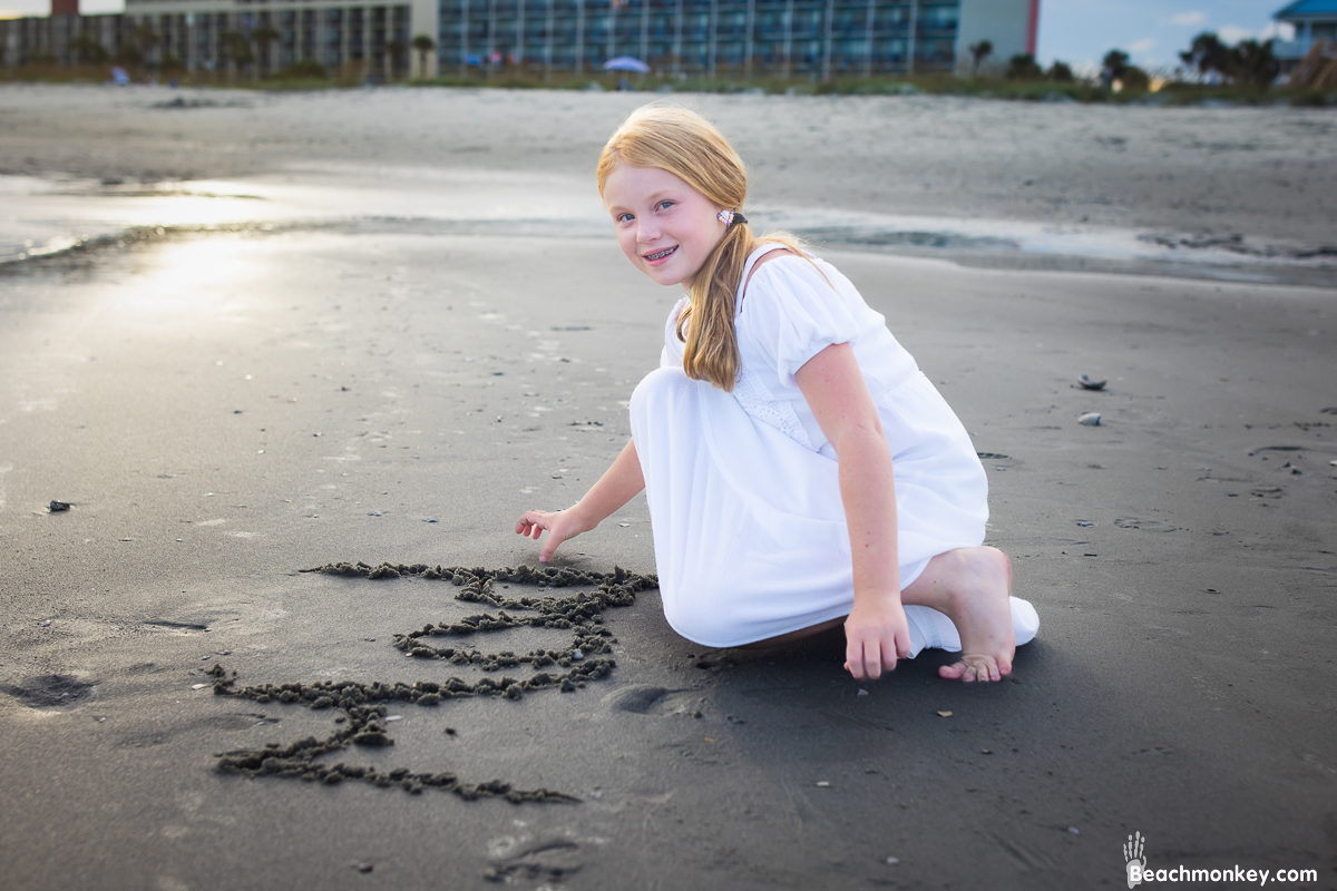 Girl writing name in sand A family Beach photo shoot in North Myrtle Beach, SC with Ashlie's family by Beachmonkey of beachmonkey photography, a family photographer on August 4th 2022