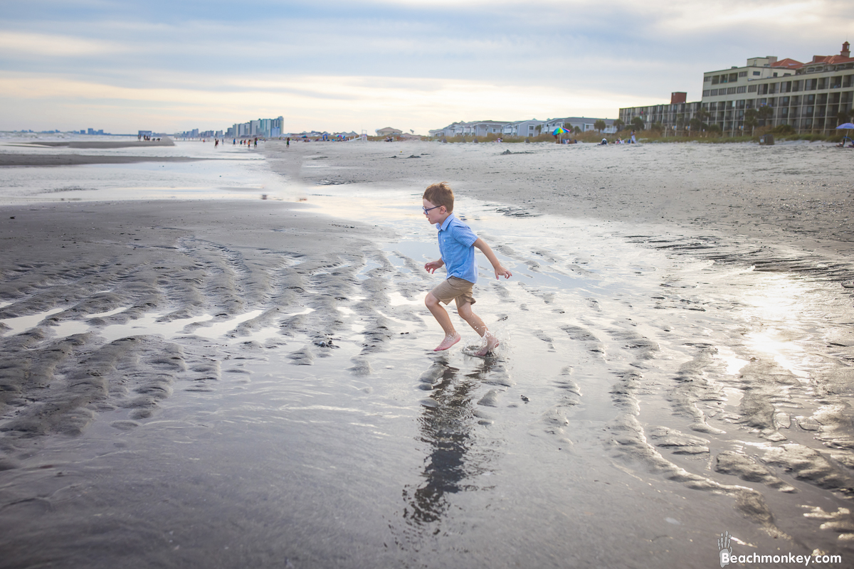 small boy running though puddle A family Beach photo shoot in North Myrtle Beach, SC with Ashlie's family by Beachmonkey of beachmonkey photography, a family photographer on August 4th 2022
