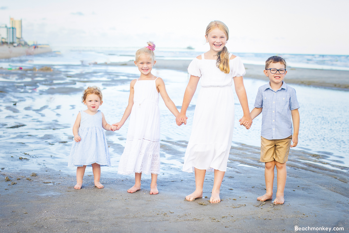 four children holding hands A family Beach photo shoot in North Myrtle Beach, SC with Ashlie's family by Beachmonkey of beachmonkey photography, a family photographer on August 4th 2022