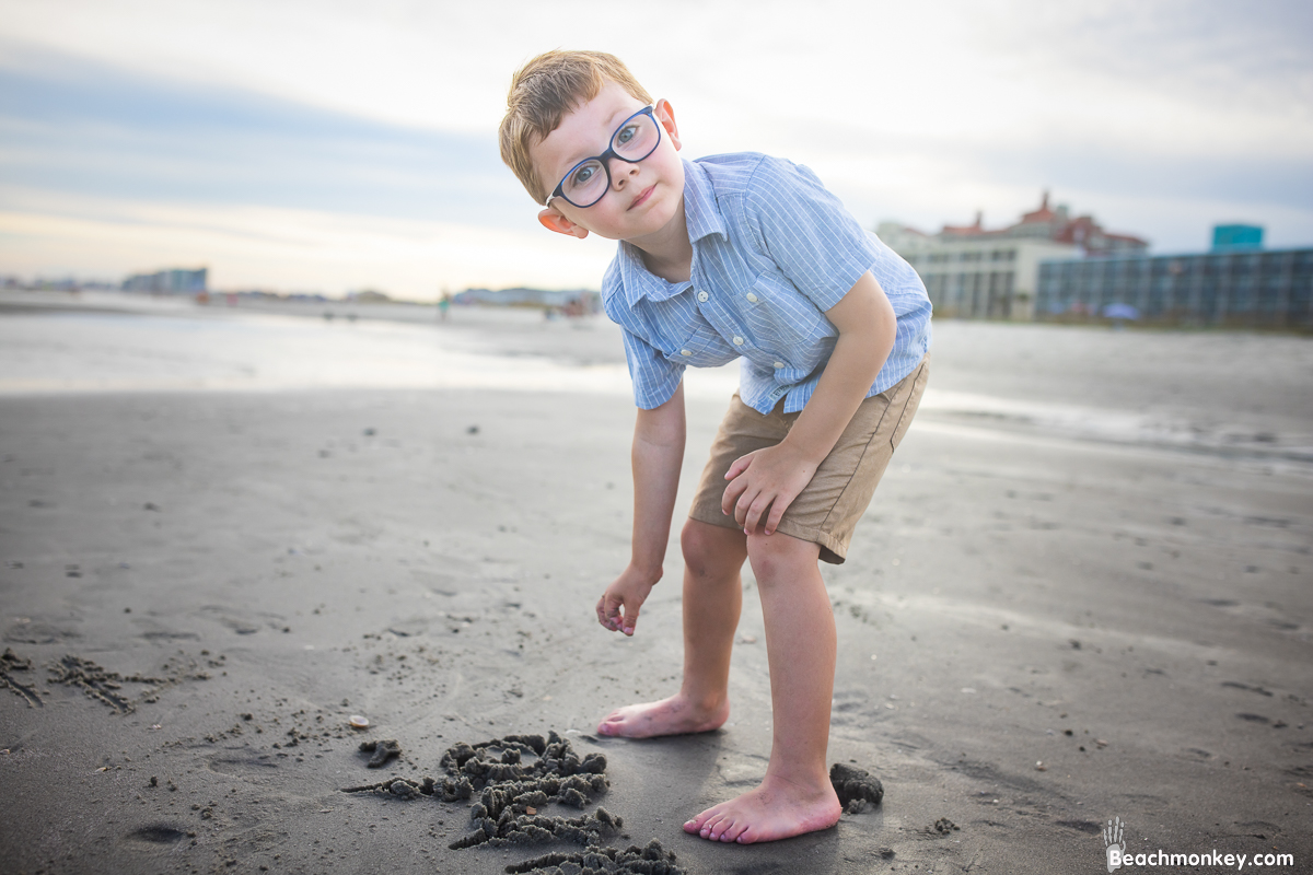 small boy writing name in sand A family Beach photo shoot in North Myrtle Beach, SC with Ashlie's family by Beachmonkey of beachmonkey photography, a family photographer on August 4th 2022