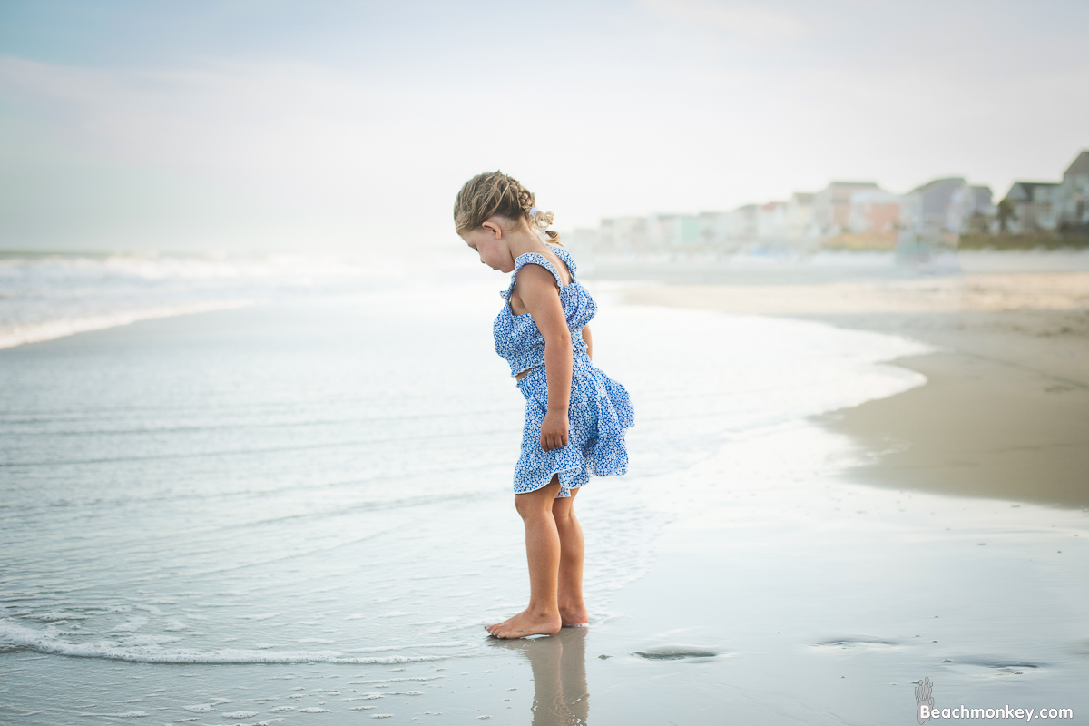 child looking at reflection in ocean at A family photo shoot in Garden City, SC at the Garden City Pier with Deanna's family by Slava of beachmonkey photography, a family photographer July 2022