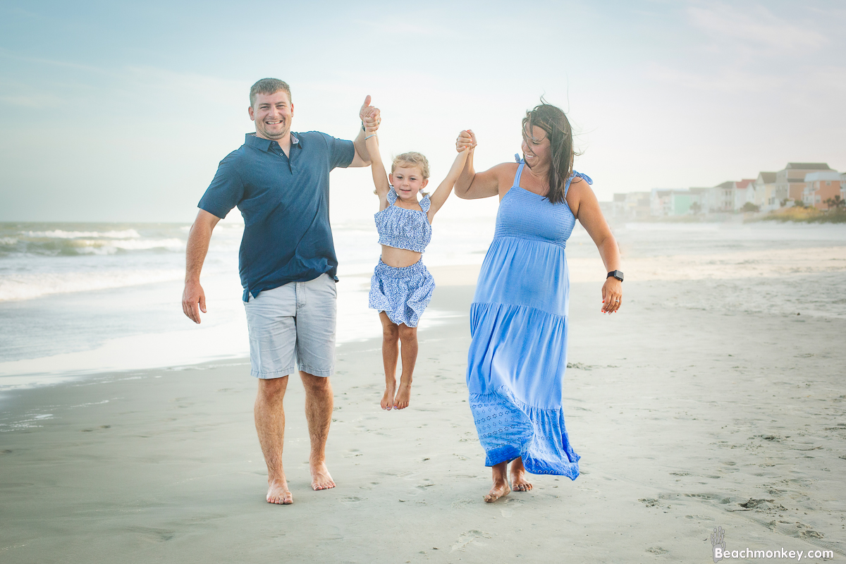 child swinging between parents A family photo shoot in Garden City, SC at the Garden City Pier with Deanna's family by Slava of beachmonkey photography, a family photographer july 2022