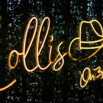 Orange neon cursive sign glowing against a dark leafy background, close-up.